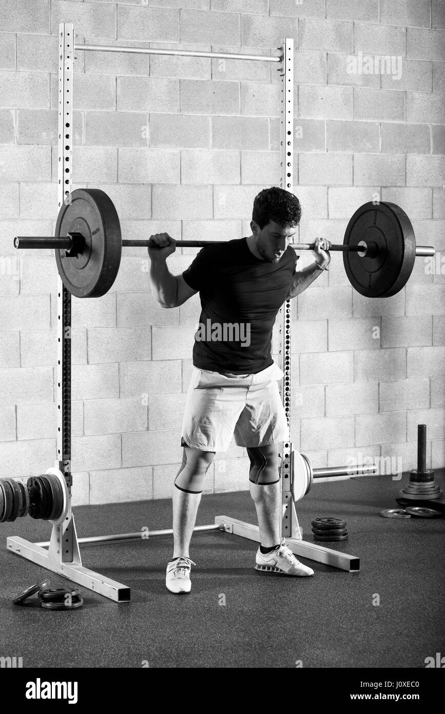 Montare atleta maschio completando un back squat in un esercizio crossfit come egli solleva un barbell pesare sulle sue spalle da una posizione di squat con un montante stan Foto Stock