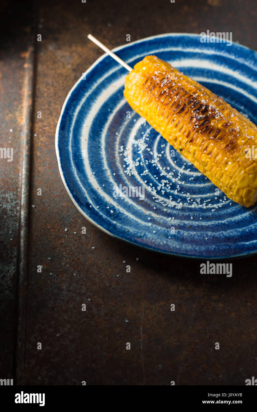Mais tostato con sale sulla ceramica blu verticale della piastra Foto Stock