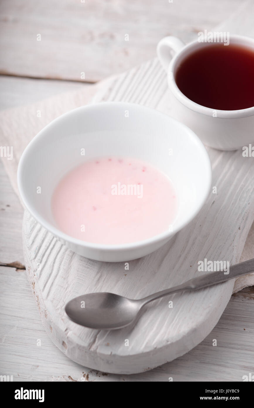 Yogurt alla frutta e la tazza di tè sul bianco tavolo in legno Foto Stock