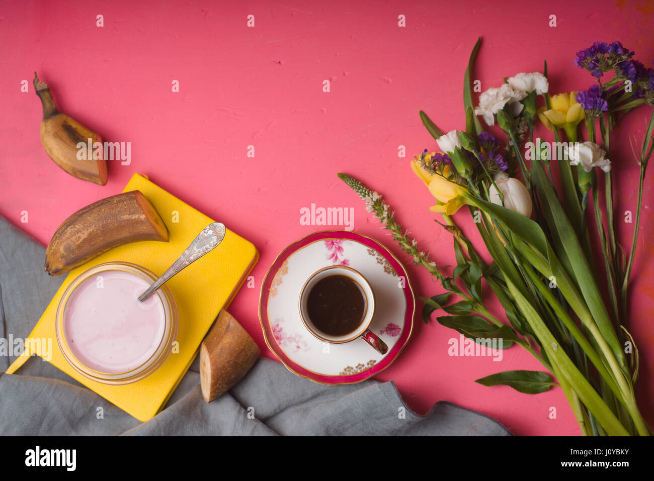 Bouquet di fiori, yogurt, una tazza di caffè su una tabella di colore rosa Foto Stock