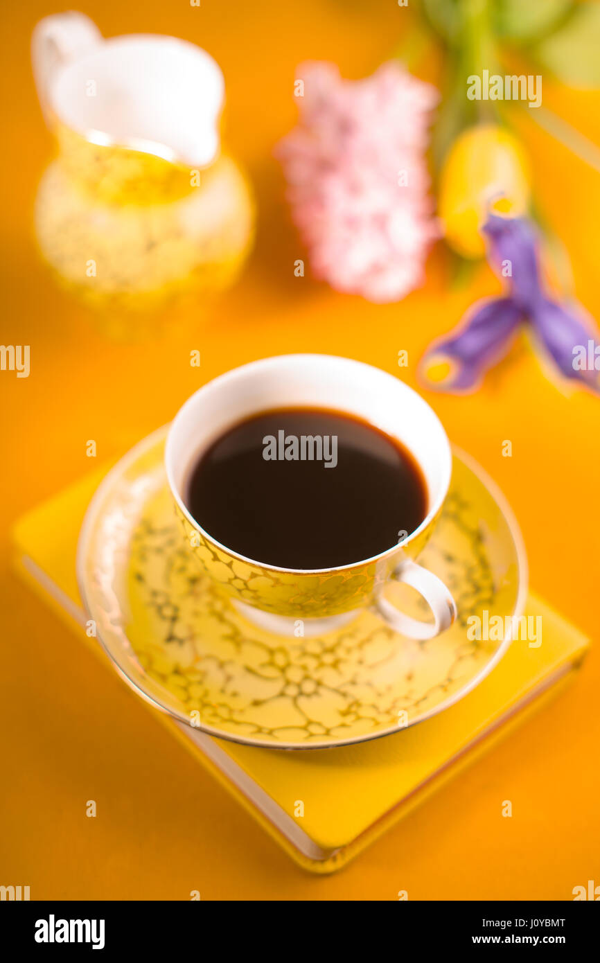 Tazza di caffè, fiori, notebook su sfondo giallo Foto Stock