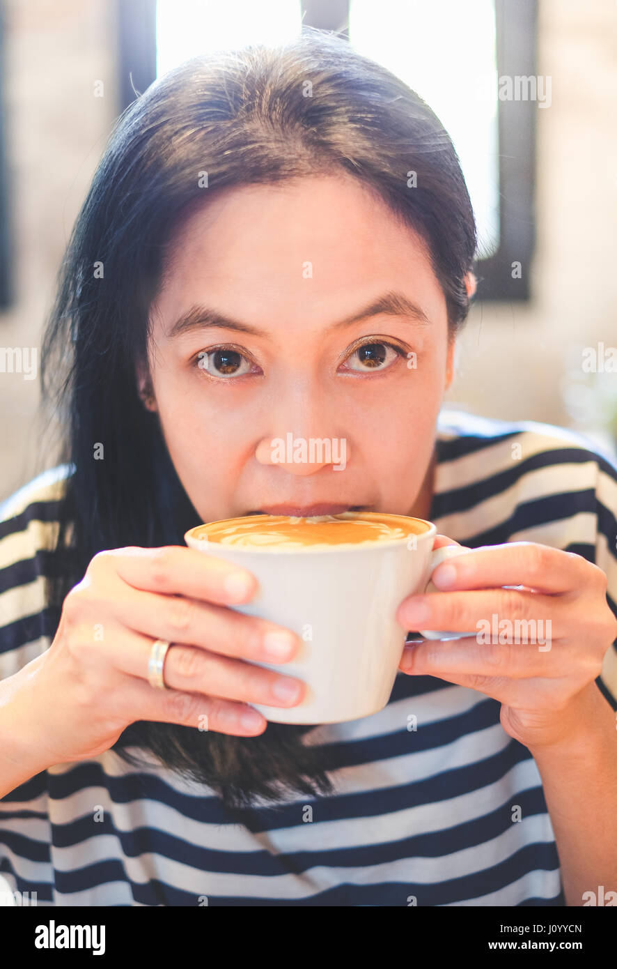 Close up volto di donna asiatica sip cappuccino caldo caffè nella caffetteria negozio,bere bevande calde. Foto Stock