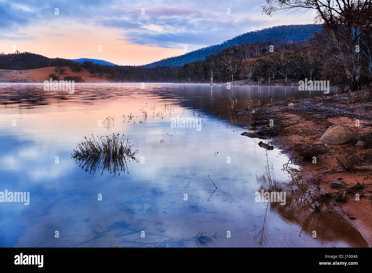 Rosa tramonto sul cambiamento delle colline intorno al lago Jindabyne in Snowy Mountains National Park in Australia. Rising Sun riflette ancora in acqua del lago d'inverno. Foto Stock
