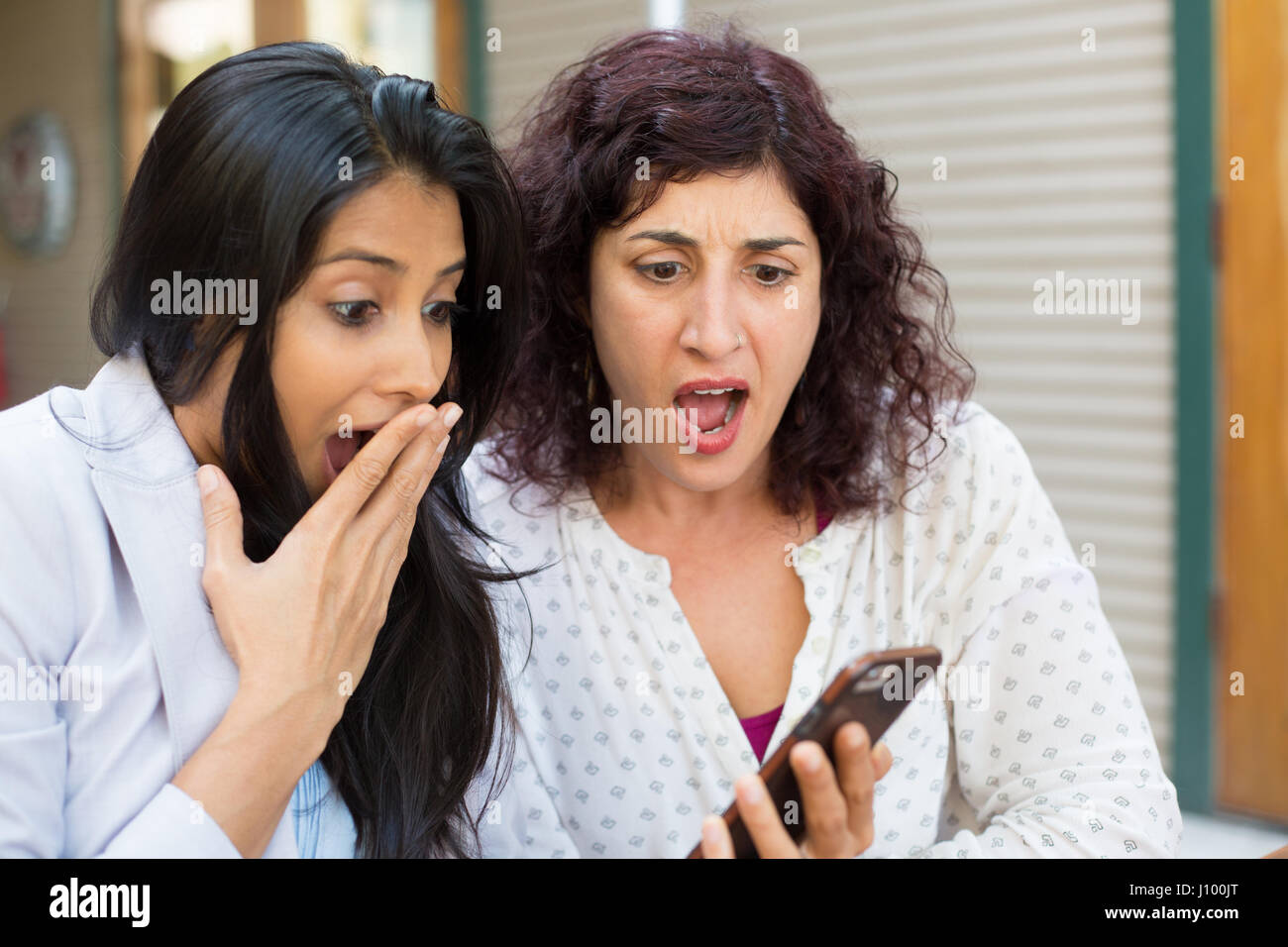 Closeup ritratto di due ragazze sorpreso guardando il telefono cellulare discutendo Ultime notizie news, shopping, molto meravigliato a ciò che vedono, isolata all'esterno Foto Stock