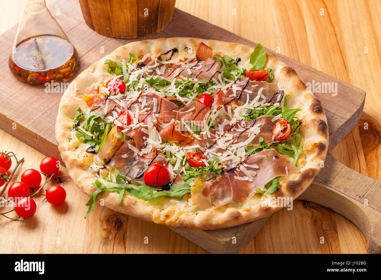 Pizza con prosciutto, rucola, pomodoro e formaggio parmigiano su un tagliere. Foto Stock