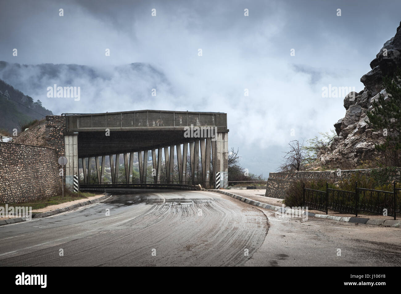 Strada di Montagna di calcestruzzo con struttura a tunnel in nebbioso giorno piovoso, rurali paesaggio di viaggio Foto Stock