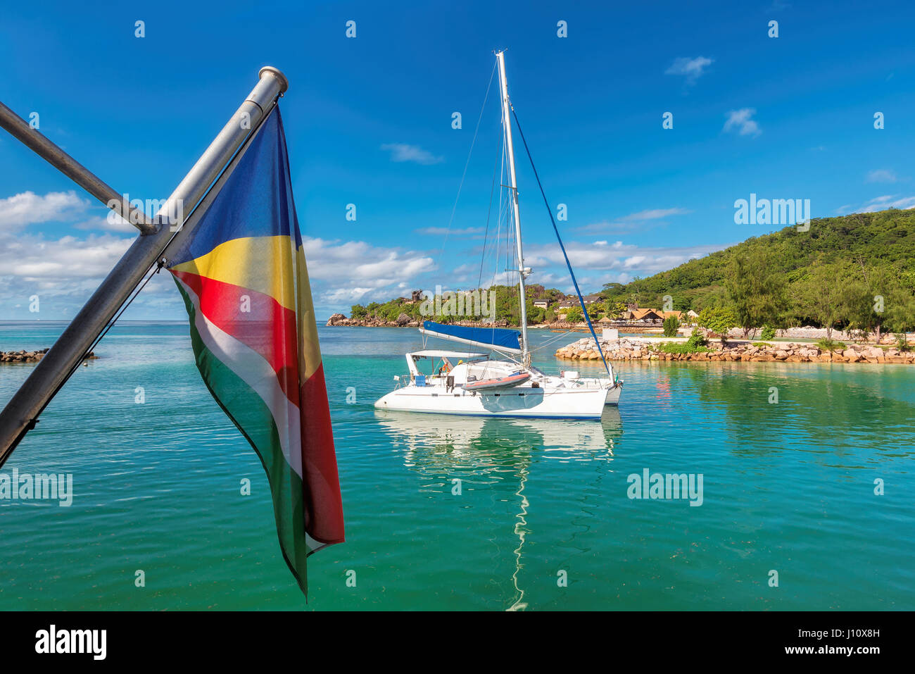 Isola tropicale con yacht a vela e bandiera delle Seychelles. Foto Stock