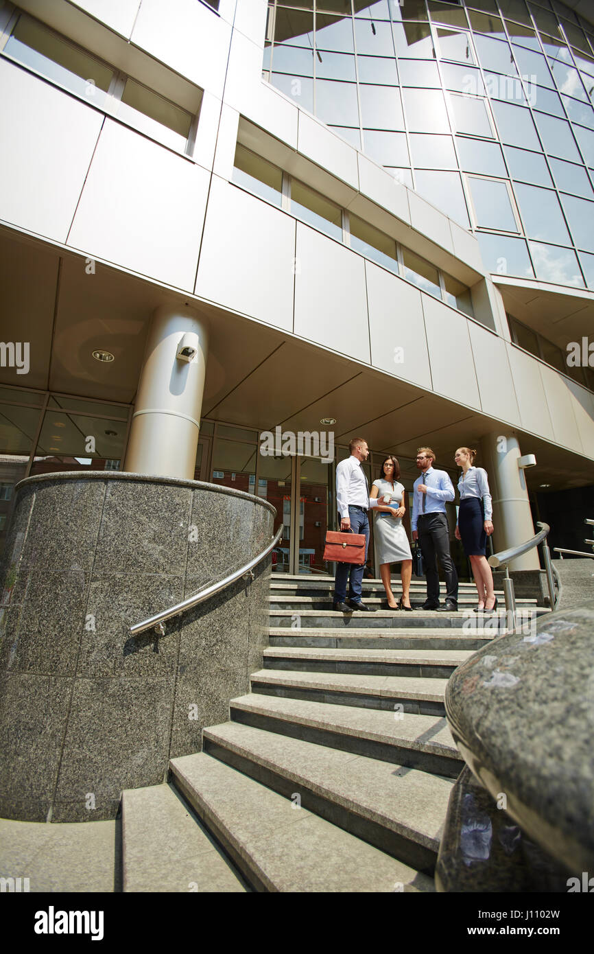 Un gruppo di persone di affari in piedi sui gradini di un ufficio moderno edificio con facciate in vetro e avvolgimento di scale in pietra Foto Stock