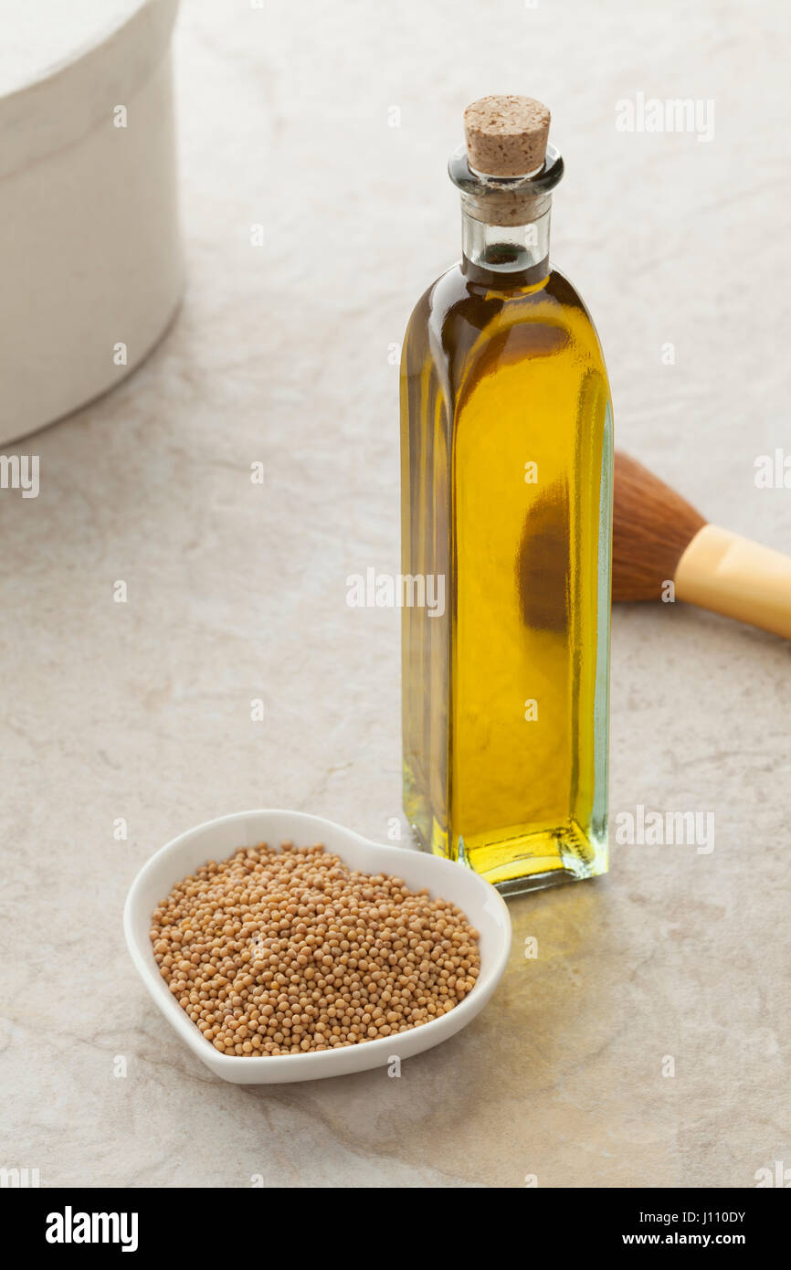 Bottiglia di vetro con olio di senape e un piatto con i semi per la cura della pelle Foto Stock