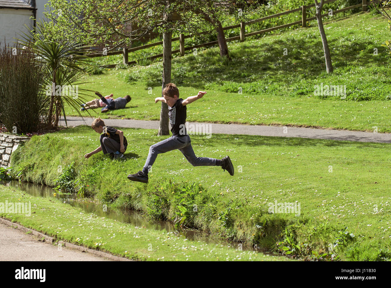 Ragazzo saltando su un flusso bambino ragazzi giocare sforzo fisico energetic energia Park Brook infanzia sfida e avventura Foto Stock