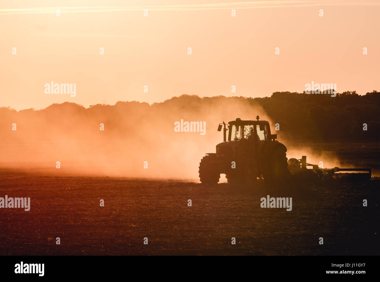 Silhouette di trattore lavora in una fattoria al crepuscolo Foto Stock