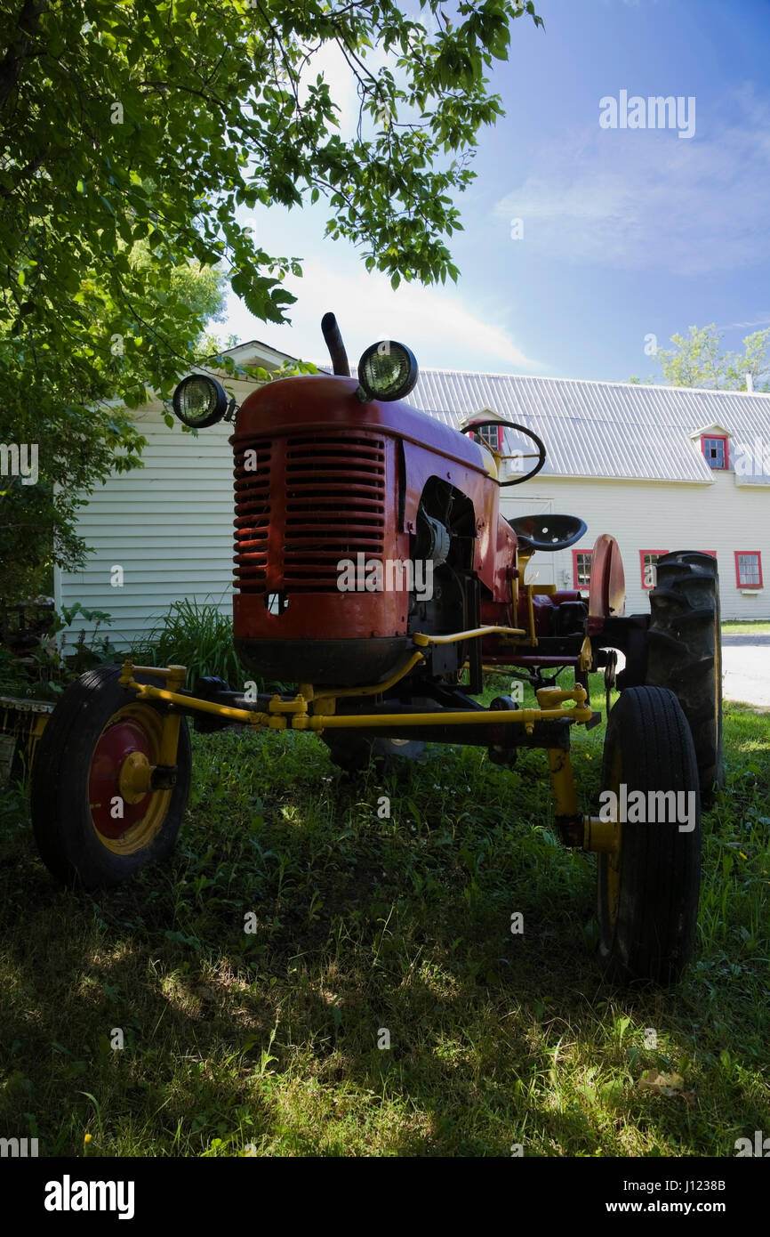 Parcheggiato vecchio rosso e giallo Fattoria Il trattore di fronte a un white barn Foto Stock