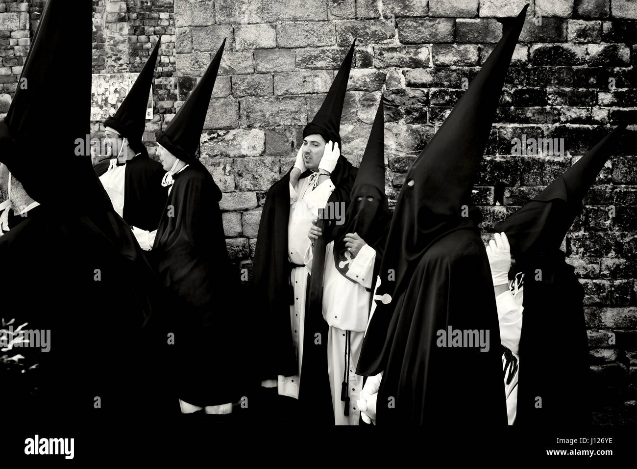 Vicini di Bossost vestito come penitenti rimanere accanto alla chiesa momenti prima di iniziare la processione del Venerdì santo per le strade dei Pirenei Foto Stock