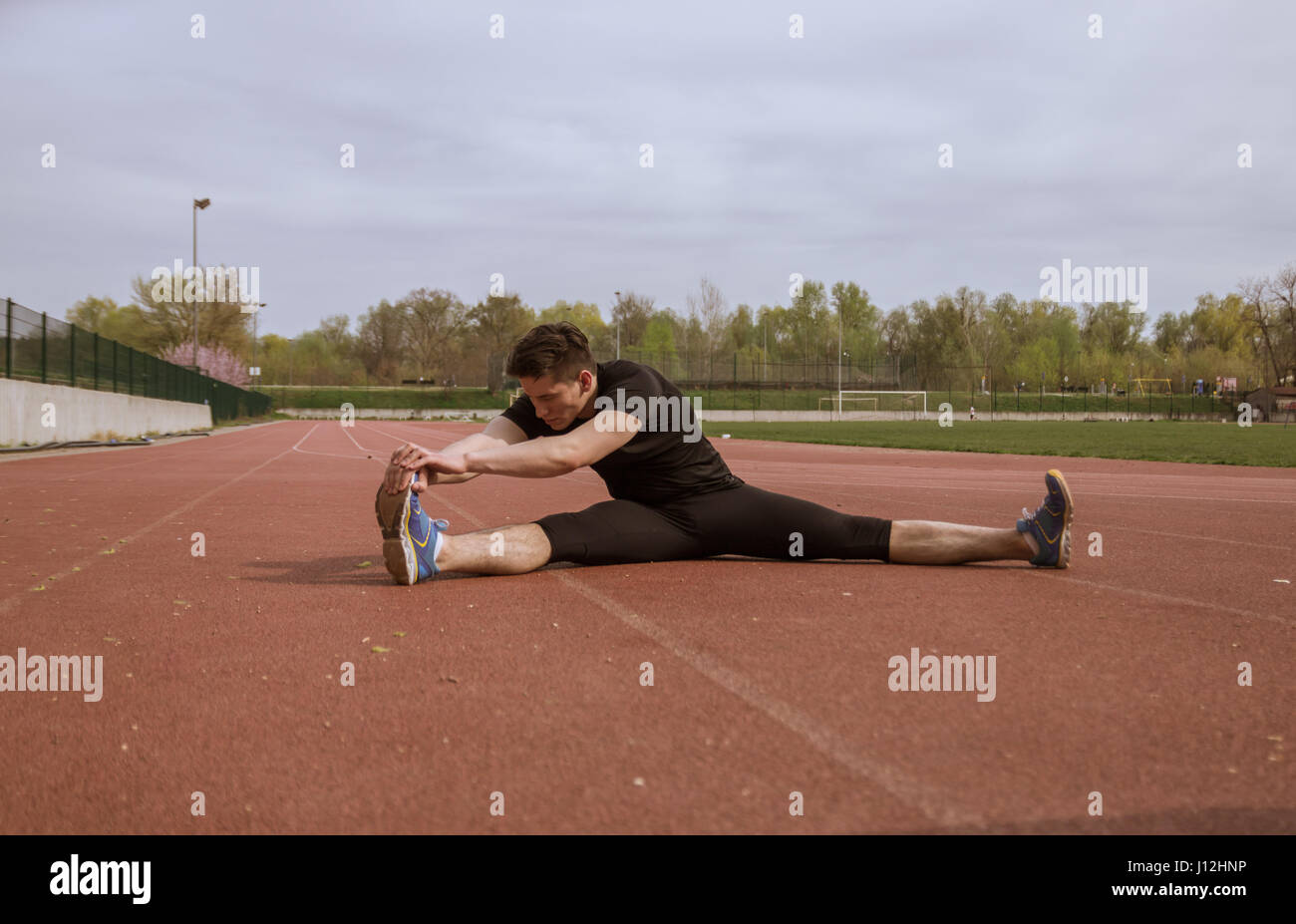 Un giovane uomo, stretching gamba, rosso acceso le vie, all'aperto, vestiti di nero Foto Stock