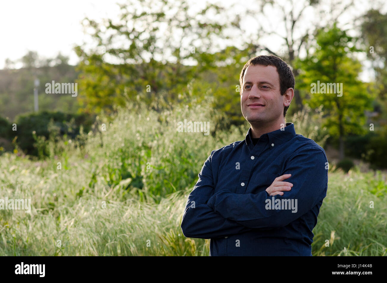 Uomo sorridente guardando al futuro in un campo erboso con le braccia incrociate. Foto Stock