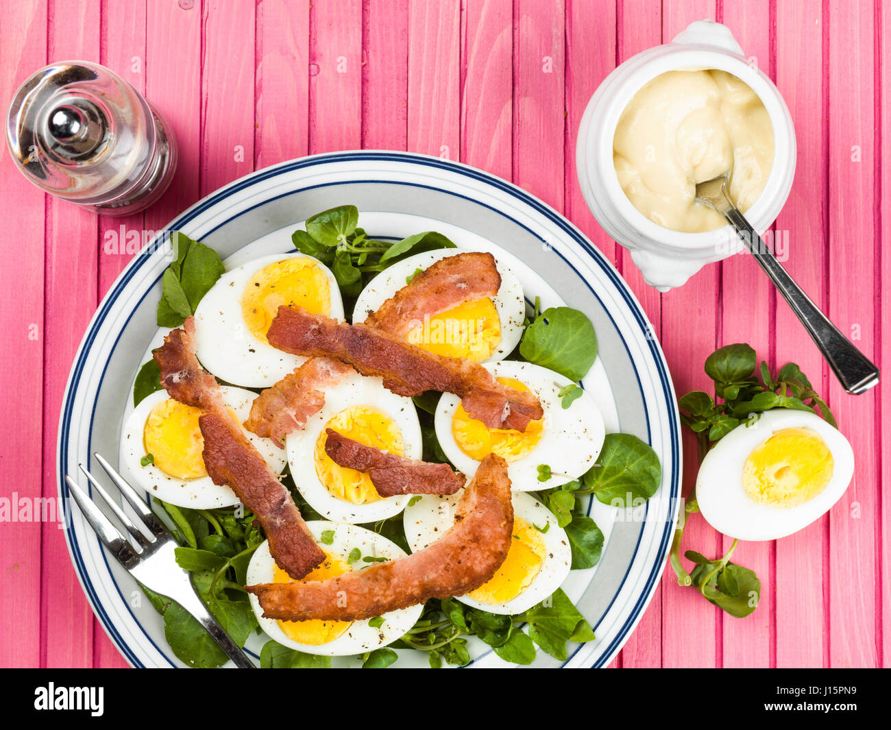 Uova e pancetta croccante con insalata di crescione contro un sfondo rosa Foto Stock