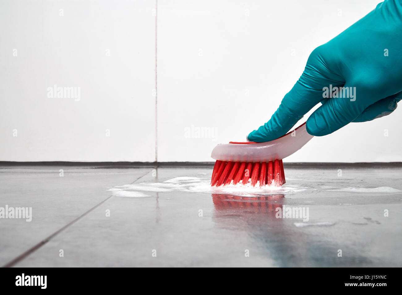 Maschio di mano con pennello rosso la pulizia del bagno piastrelle sul pavimento. Foto Stock