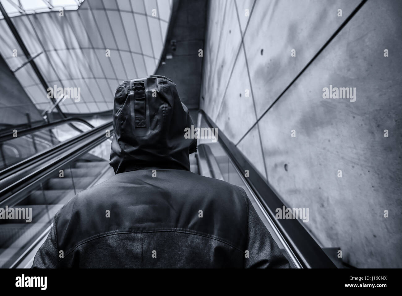 Irriconoscibile incappucciati persona sullo spostamento di escalator in moderno urbano circostante interno,immagine monocromatica con il fuoco selettivo Foto Stock