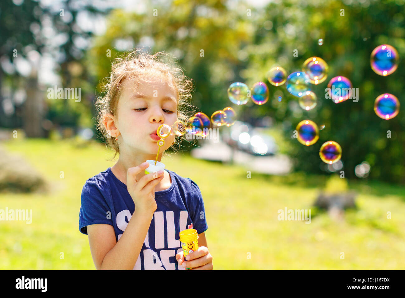 Una bambina soffiando bolle di sapone in estate park. Sfondo per la tonificazione instagram filtro. Foto Stock