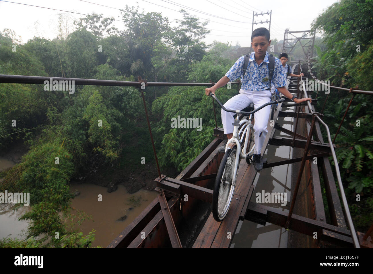 JAVA, INDONESIA: Equilibratura su dieci pollici di larghezza doghe in legno questi bambini devono attraversare una precaria 100 piedi di lunghezza cavo in acciaio ponte mentre sulla loro BYCYCLES solo per arrivare a scuola. Se pensavate che la vostra scuola è stata un incubo un pensiero di ricambio per questi bambini che sono così dedicata alla loro educazione che essi sono disposti a rischiare la vita e arto sulla loro missione quotidiana per raggiungere l'Aula. Fotografo locale Agoes Rudianto (28) ha preso la foto di bambini che viaggiano dalla città di Boyolali, Java, Indonesia. Foto Stock