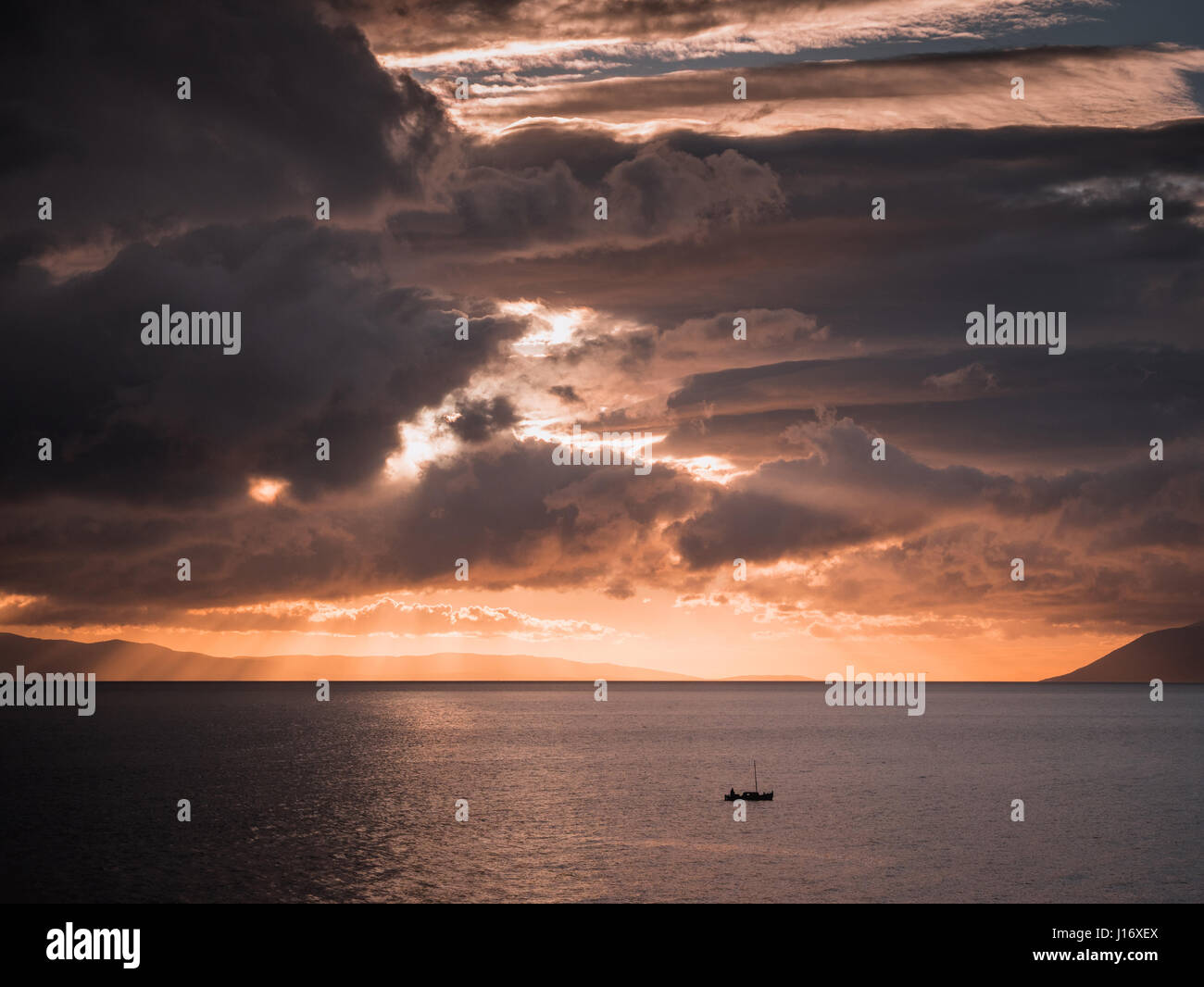 Piccola barca sul mare calmo con grandi nuvole sopra al tramonto Foto Stock