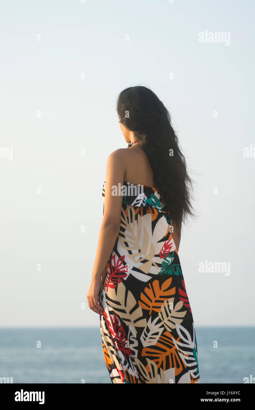 Giovane donna in piedi sulla spiaggia che guarda lontano Foto Stock