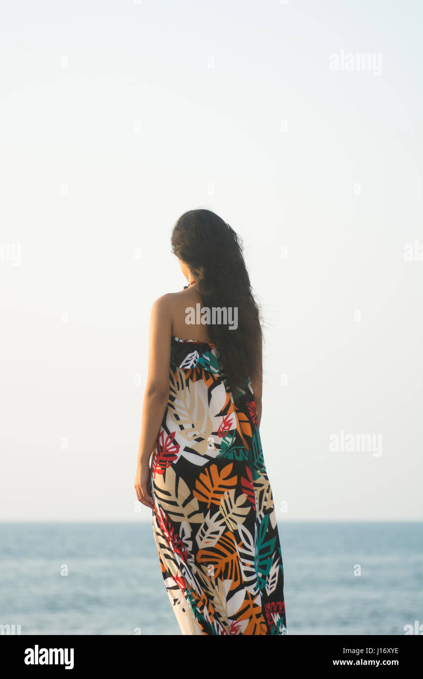 Vista posteriore di una giovane donna con i capelli scuri in piedi vicino al mare Foto Stock