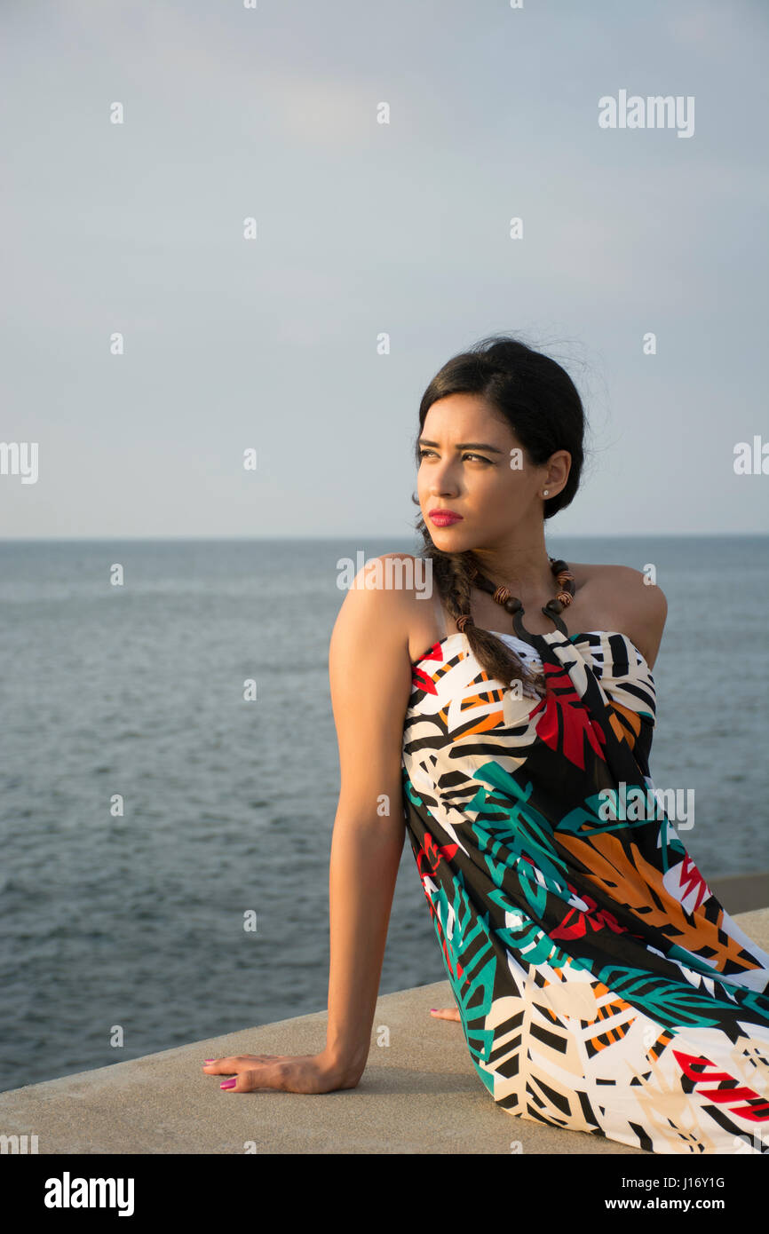 Giovane donna si pose a sedere presso il mare alla ricerca di distanza Foto Stock
