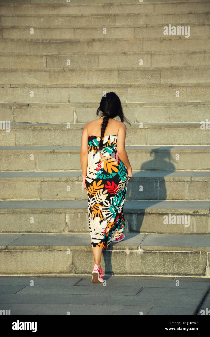 Vista posteriore di una giovane donna che indossa abiti estivi camminando su per le scale fino all'aperto Foto Stock