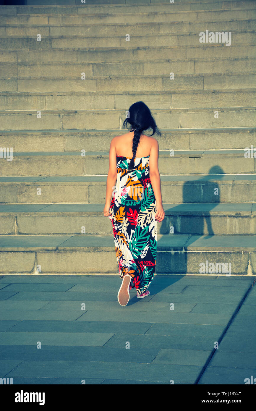 Vista posteriore di una giovane donna che indossa abiti estivi camminando su per le scale fino all'aperto Foto Stock