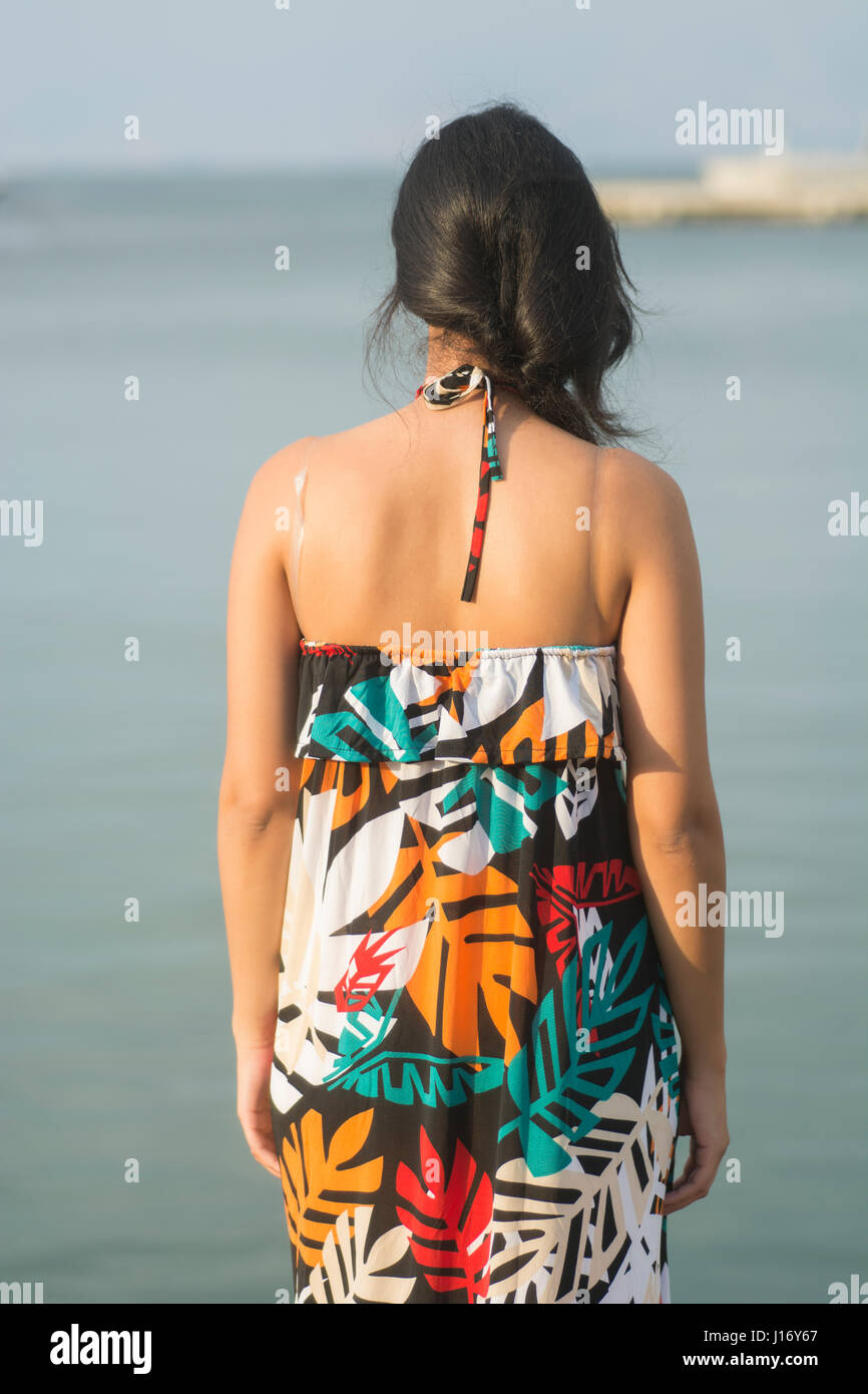Vista posteriore di una giovane donna che indossa un vestito estivo in piedi vicino al mare Foto Stock