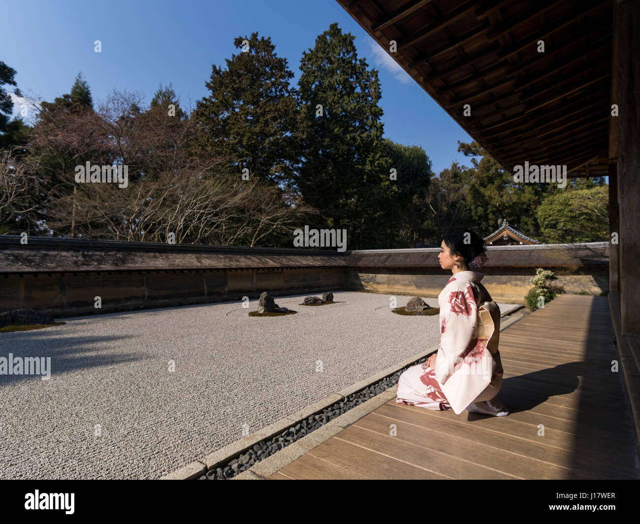 Giovane donna giapponese in kimono si inginocchia accanto al giardino di roccia a Ryoan-ji, Kyoto. Uno degli esempi più belli di un noleggio-niwa giardino di pietra. Zen meditatio Foto Stock