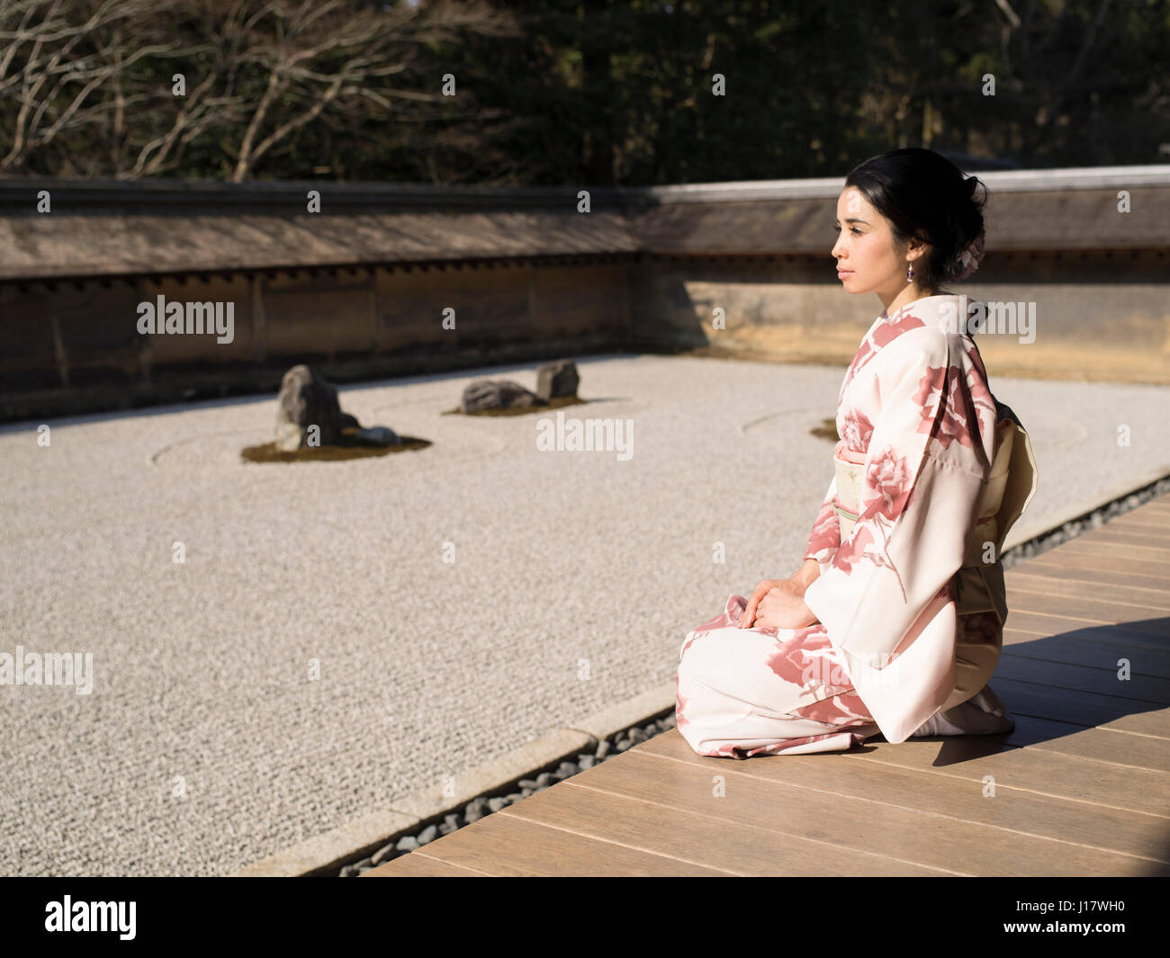 Giovane donna giapponese in kimono si inginocchia accanto al giardino di roccia a Ryoan-ji, Kyoto. Uno degli esempi più belli di un noleggio-niwa giardino di pietra. Zen meditatio Foto Stock