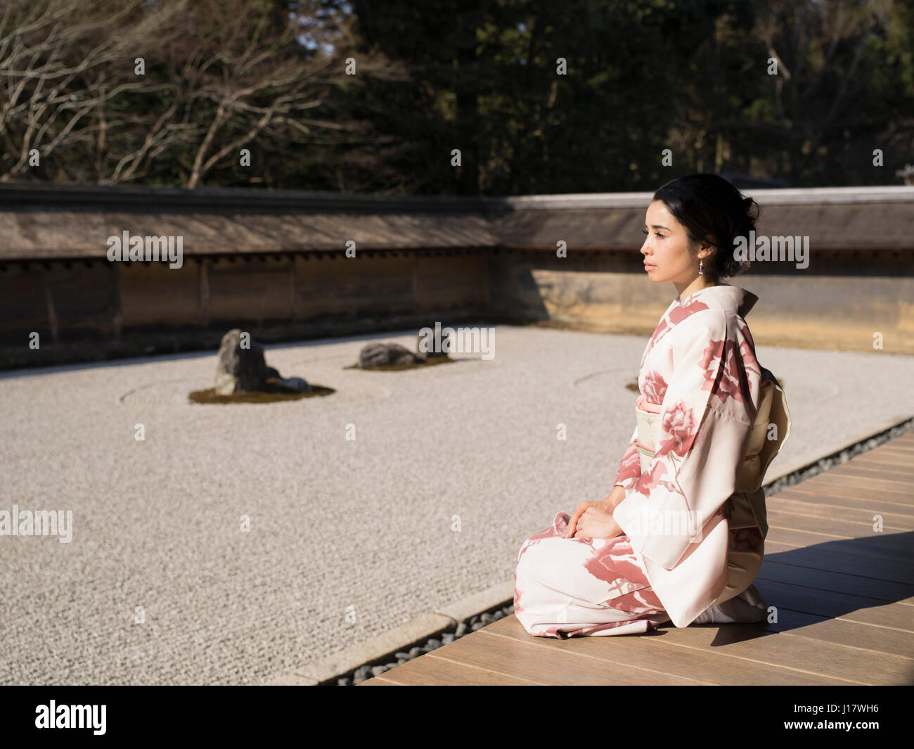 Giovane donna giapponese in kimono si inginocchia accanto al giardino di roccia a Ryoan-ji, Kyoto. Uno degli esempi più belli di un noleggio-niwa giardino di pietra. Zen meditatio Foto Stock