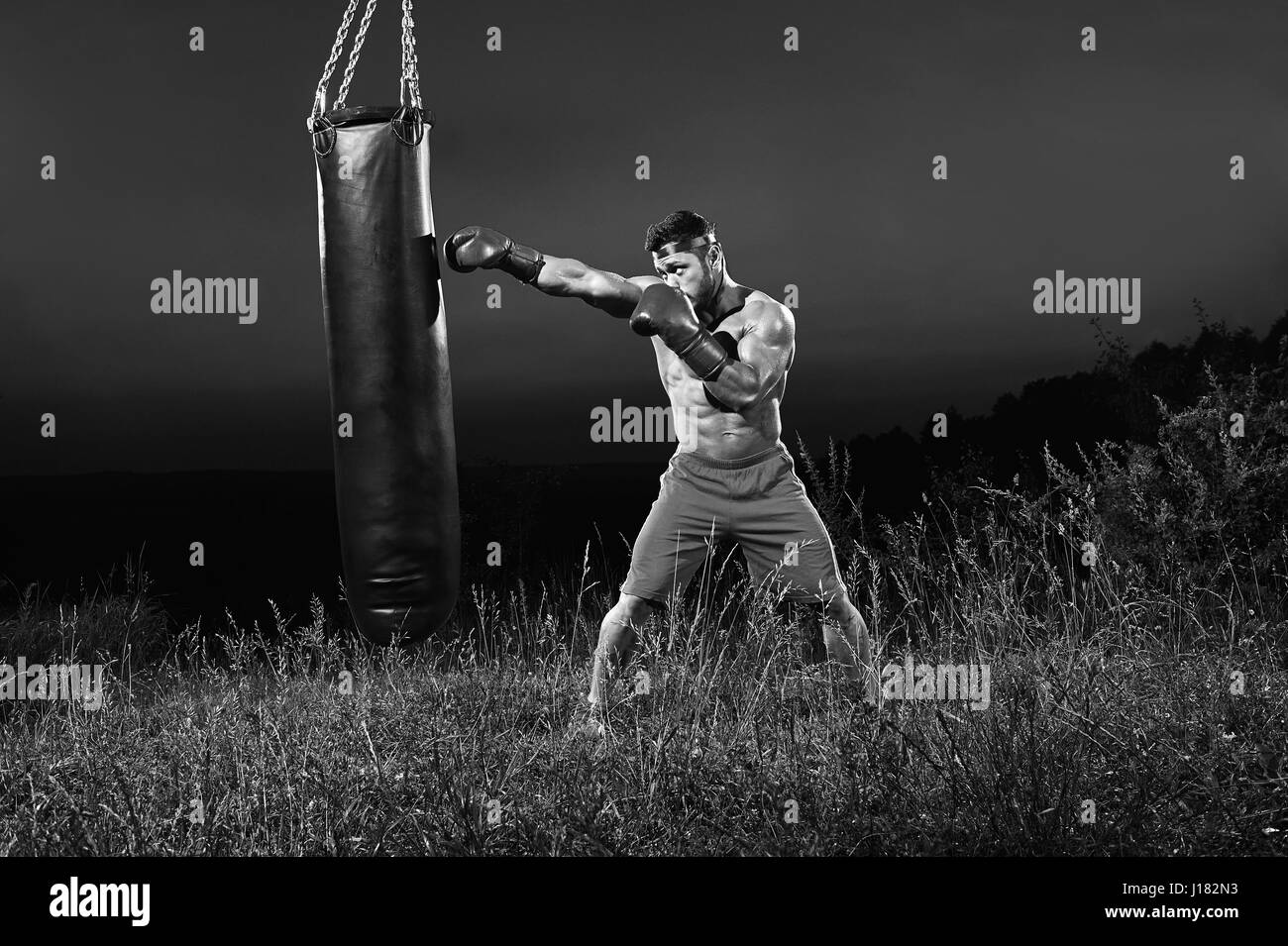 Foto in bianco e nero di un boxer maschio di formazione con un sacco da boxe ou Foto Stock