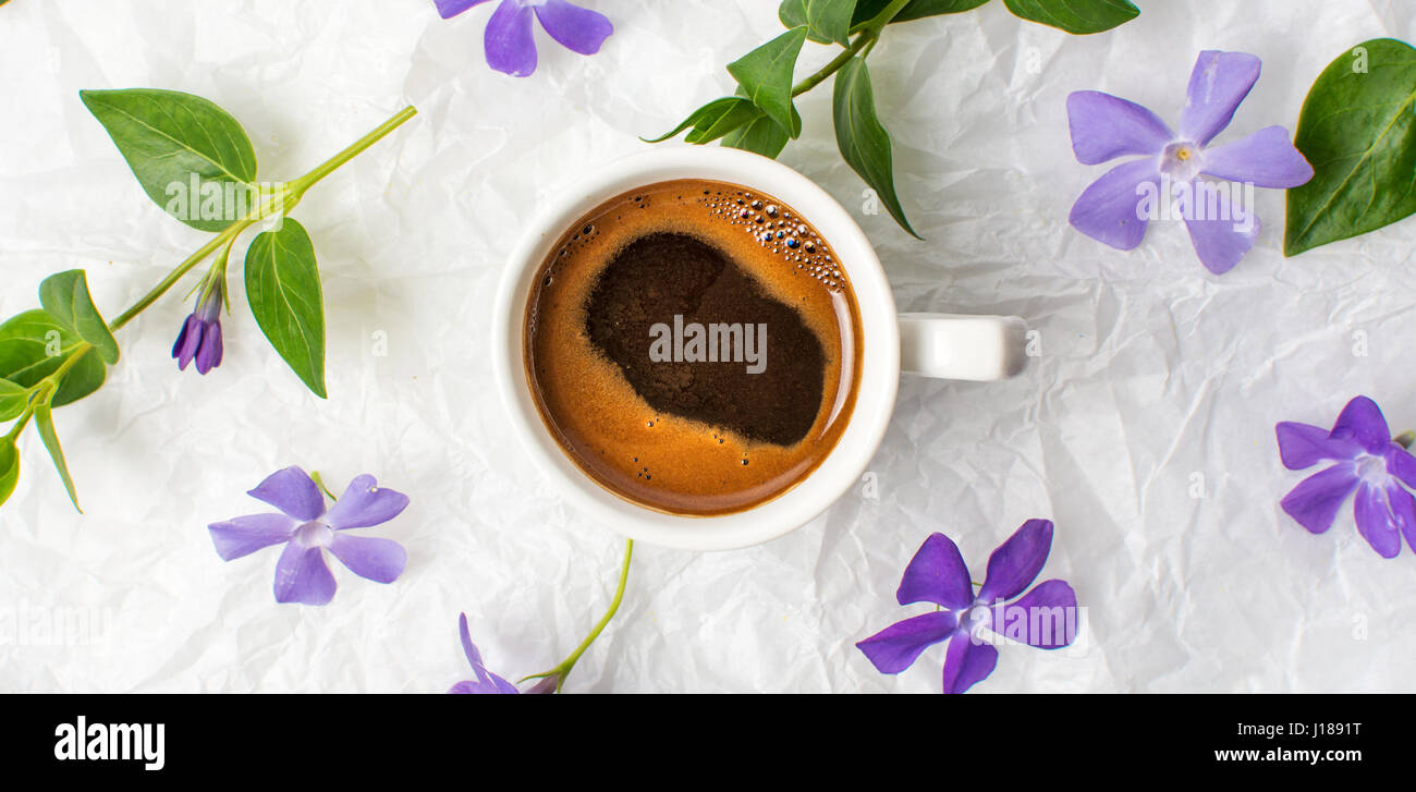 Tazza di caffè e viola fiori di primavera sulla biancheria da letto Foto Stock