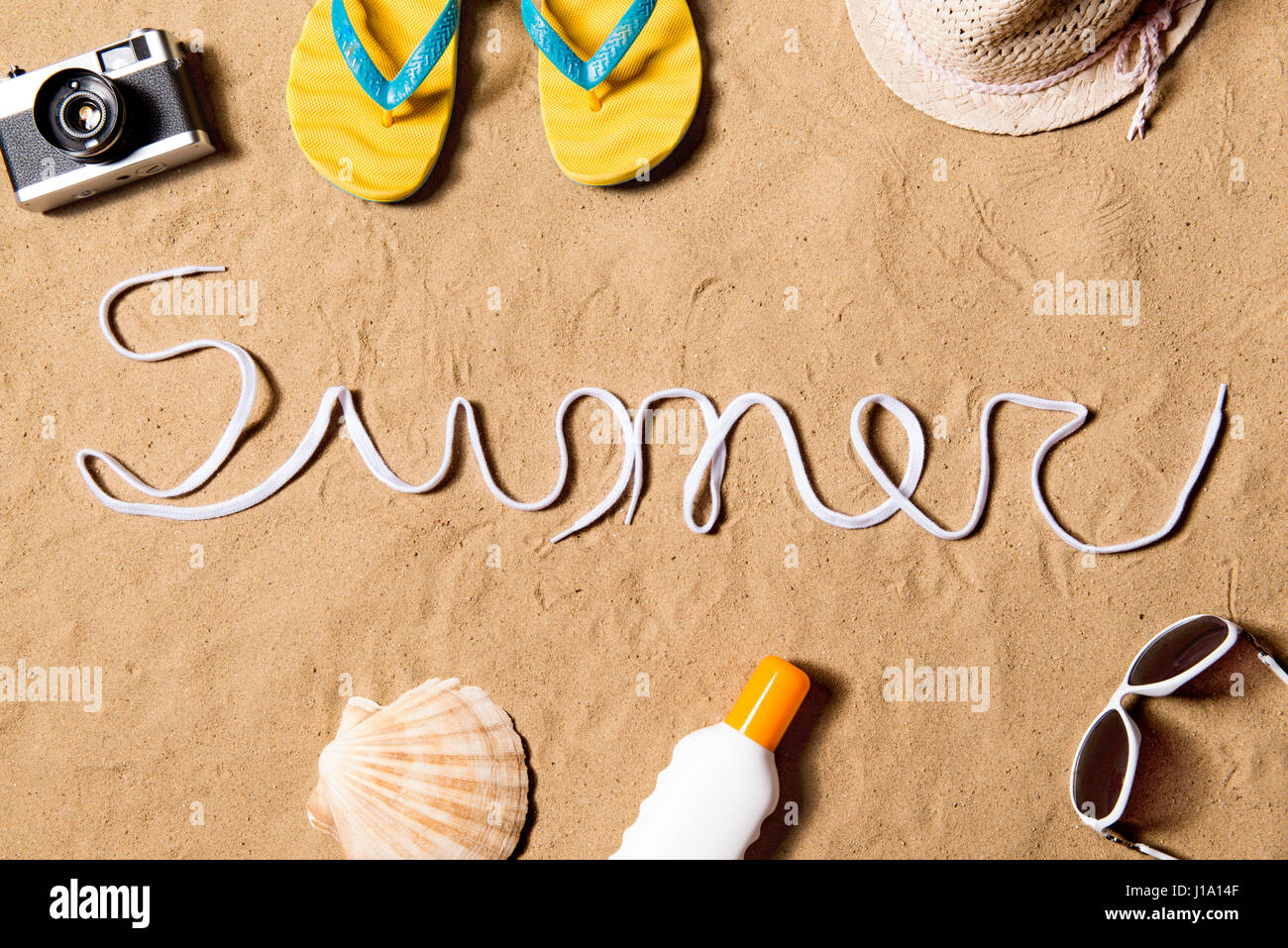 La vacanza estiva composizione. Segno di estate fatta di lacci delle scarpe, coppia di giallo flip flop sandals, cappello, occhiali da sole, crema solare e altre cose su una spiaggia. S Foto Stock