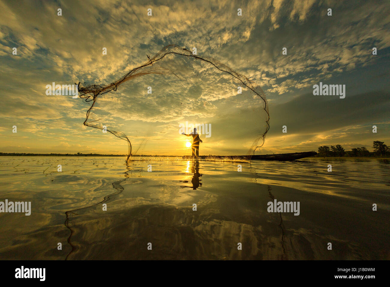 Thai pescatore sulla barca di legno di una rete di colata per la cattura di pesci di acqua dolce in natura fiume nelle prime ore della sera prima del tramonto Foto Stock