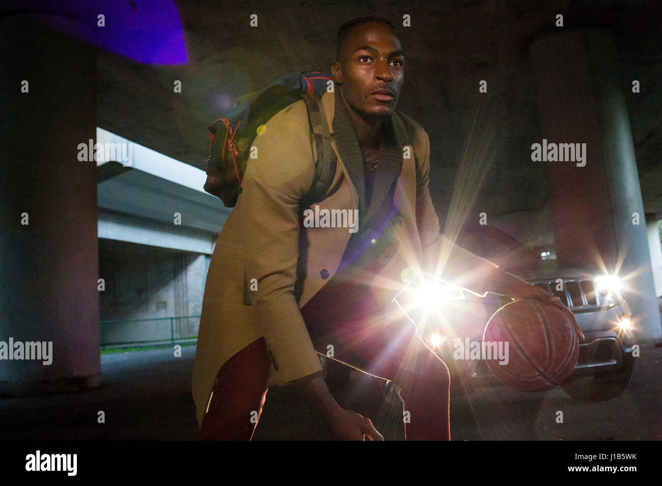 Fari anteriori che splende su uomo nero indossando uno zaino giocare a basket Foto Stock