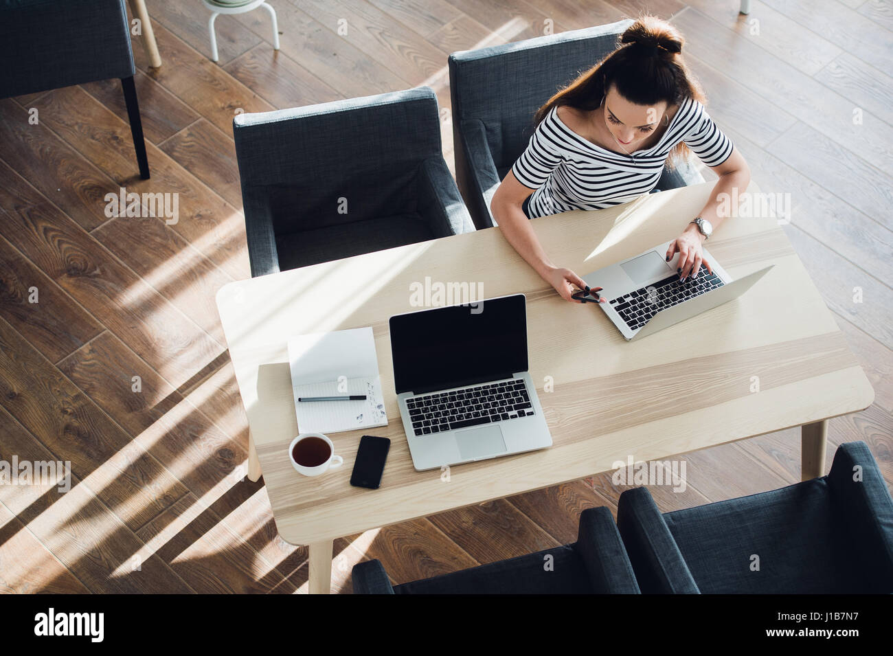 Il Multitasking donna in un cafe, lavorando sia su telefono e computer portatile, mentre il suo collaboratore di appoggio. Foto Stock