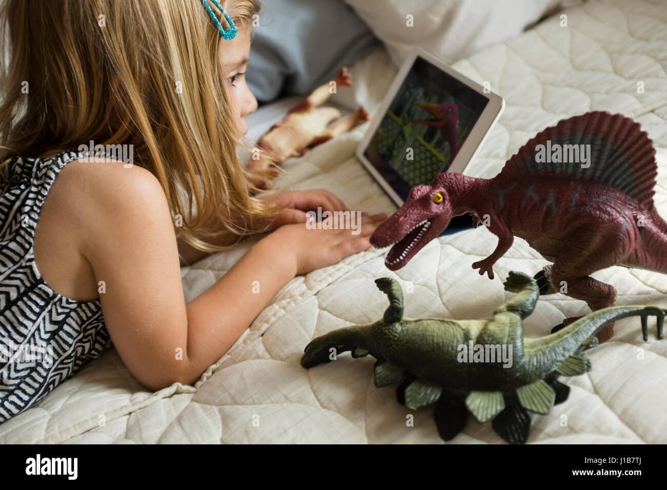 Ragazza caucasica la posa sul letto con dinosauri giocattolo con tavoletta digitale Foto Stock