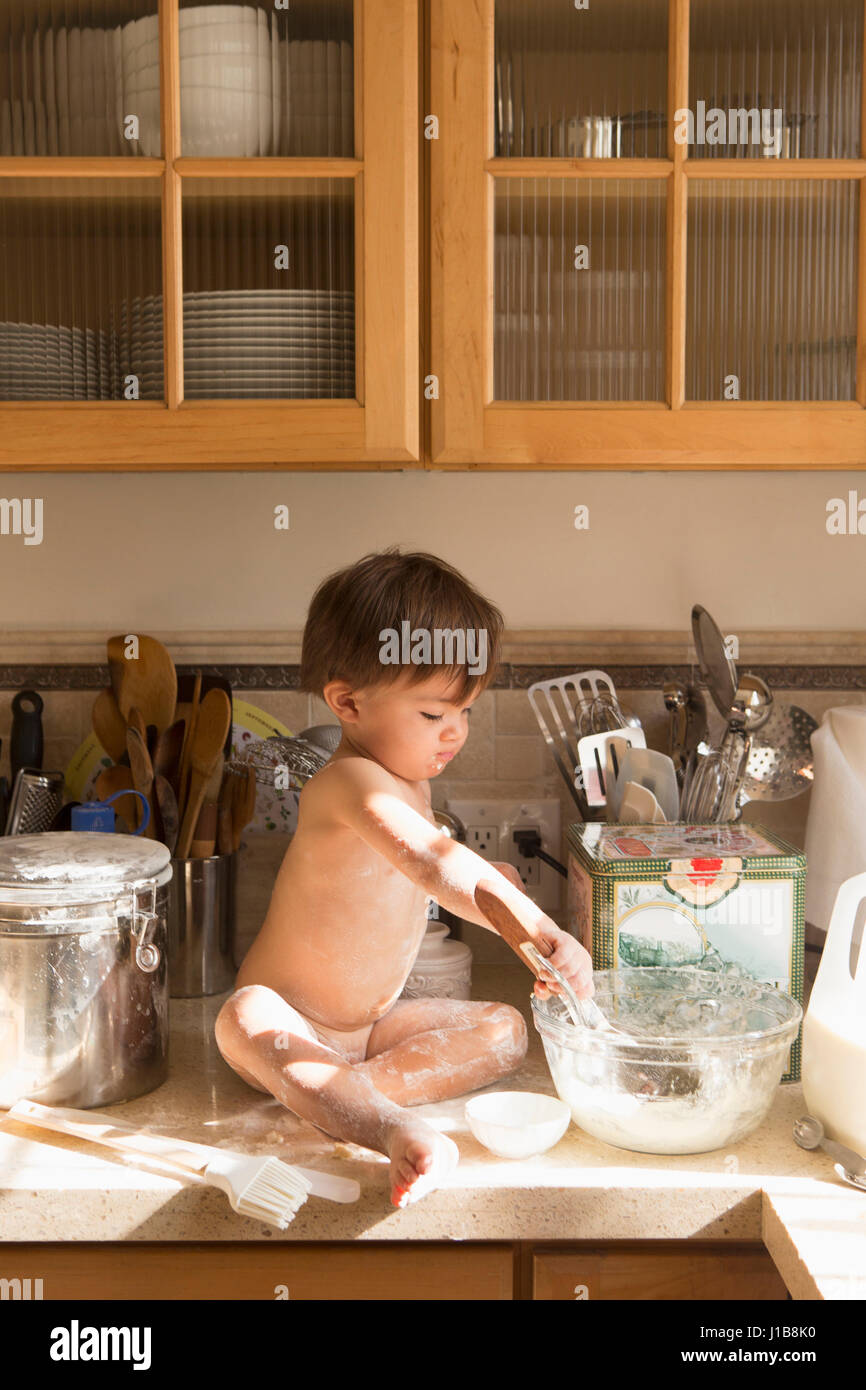 Razza mista ragazzo seduto sul bancone cucina cibo di miscelazione in un recipiente Foto Stock