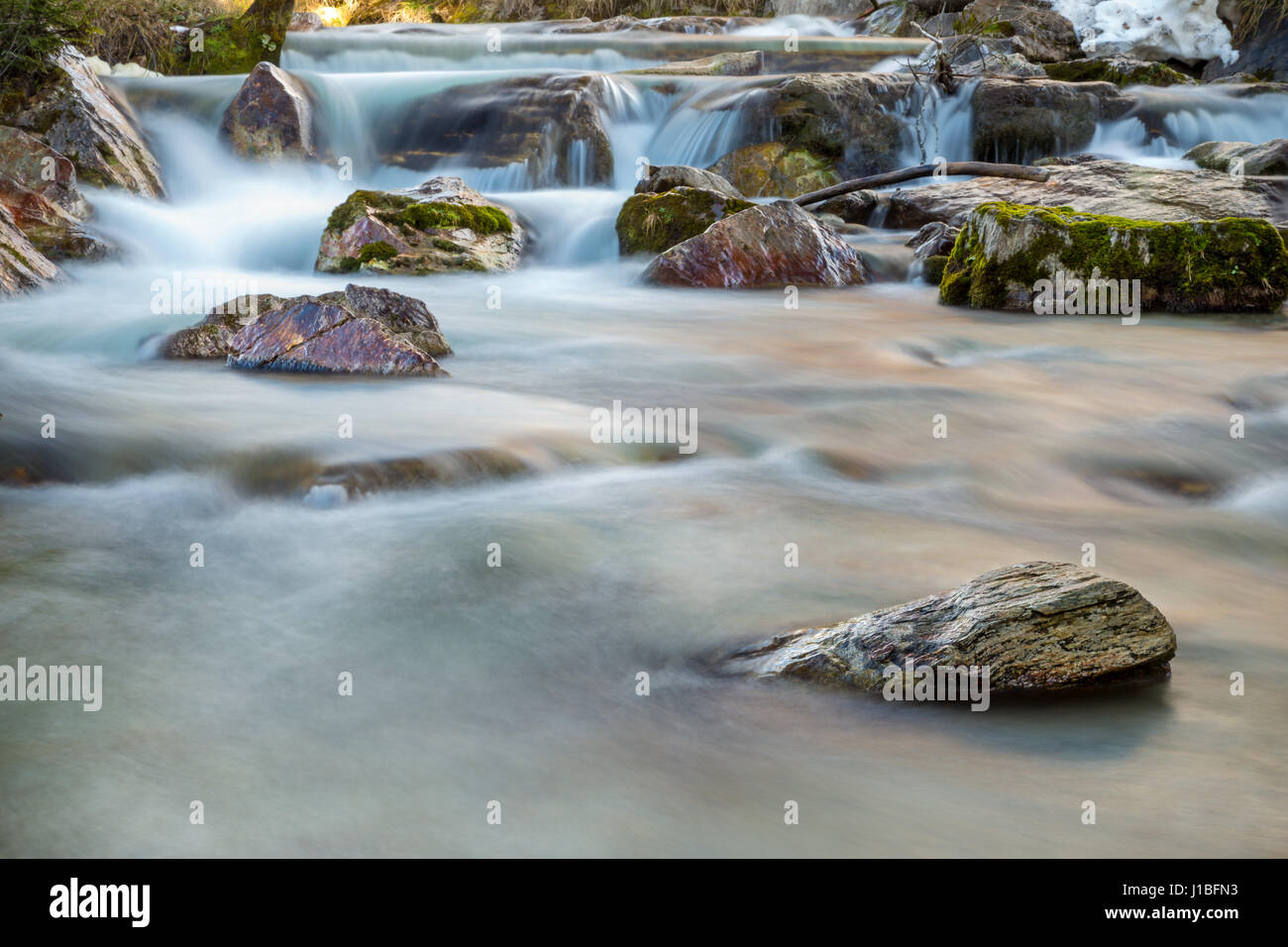 Un close-up di un piccolo ruscello di montagna. L'acqua è sfocato mentre le rocce sporgenti spiccano. Foto Stock