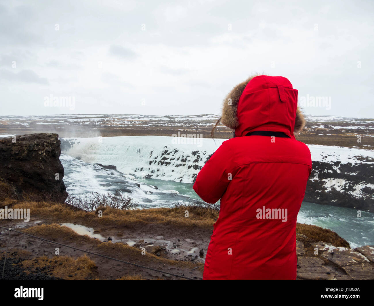 Una donna che indossa un cappotto rosso si affaccia sulla cascata di Gullfoss nel sud-ovest dell'Islanda Foto Stock