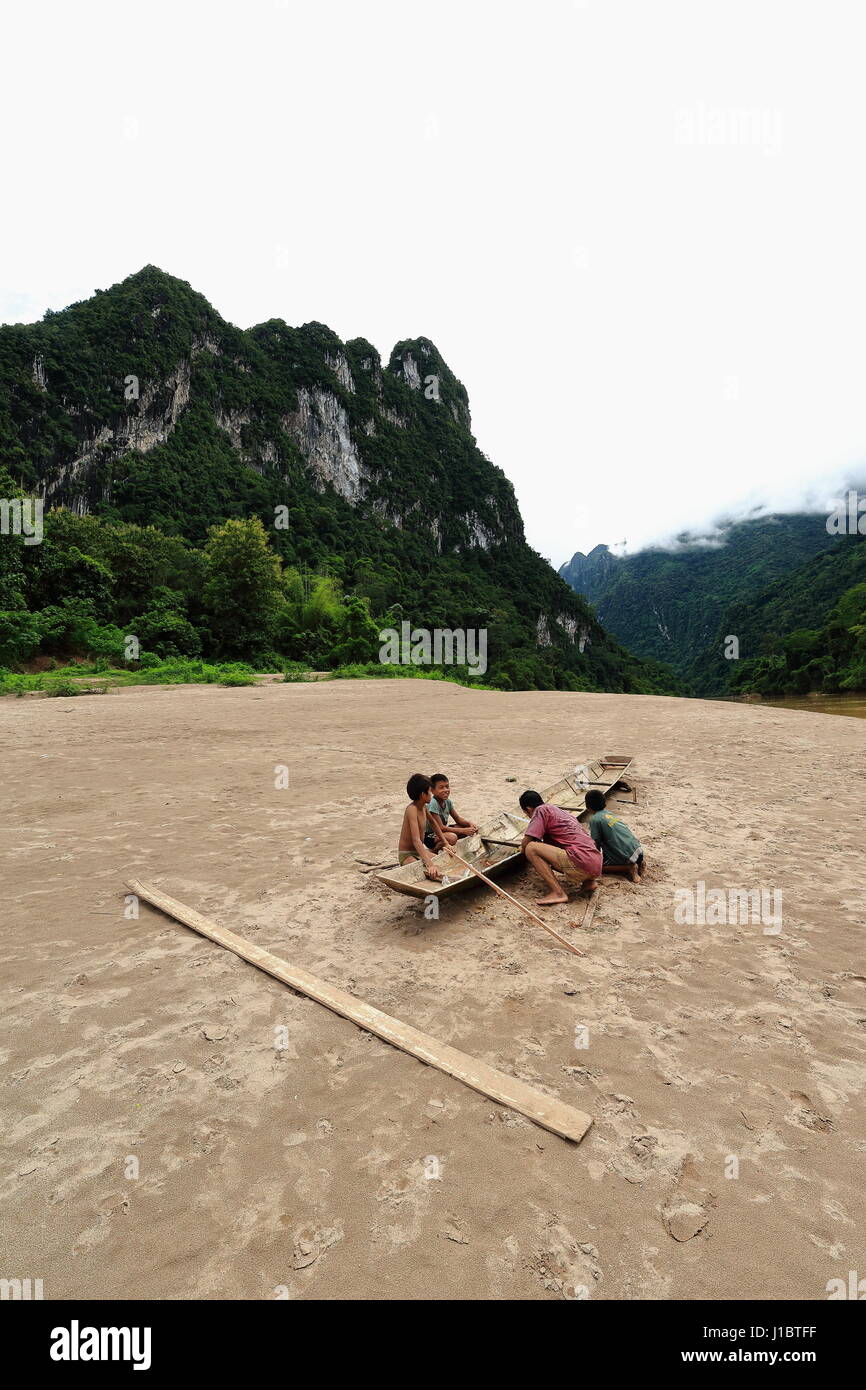 Nam Ou river, Laos-October 9, 2015: slowboats locali percorrono il fiume che serve come principale mezzo di trasporto in mancanza di terra di strade. Boatman riparazioni la sua fila Foto Stock