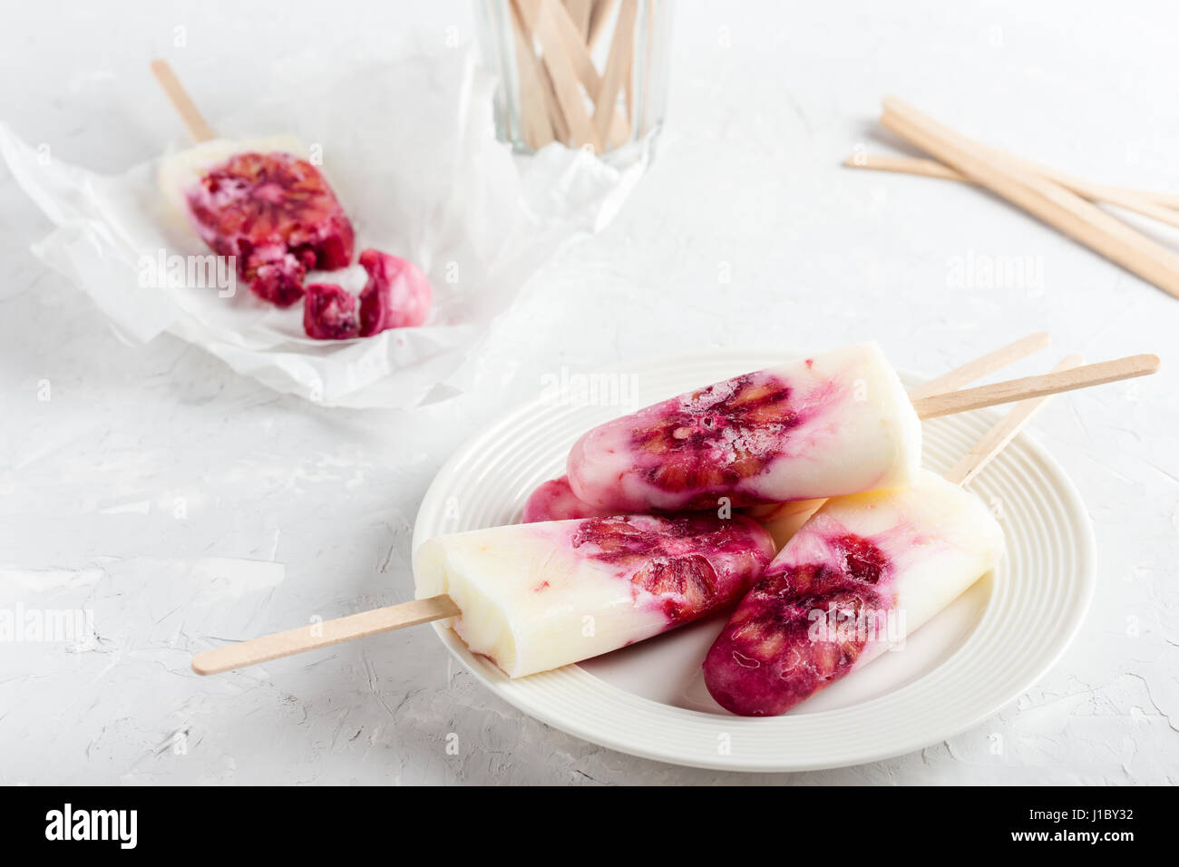 Yogurt fatto in casa ice pops decorate con sangue fettine di arancia sulla piastra bianca su di colore grigio chiaro nella tabella Foto Stock