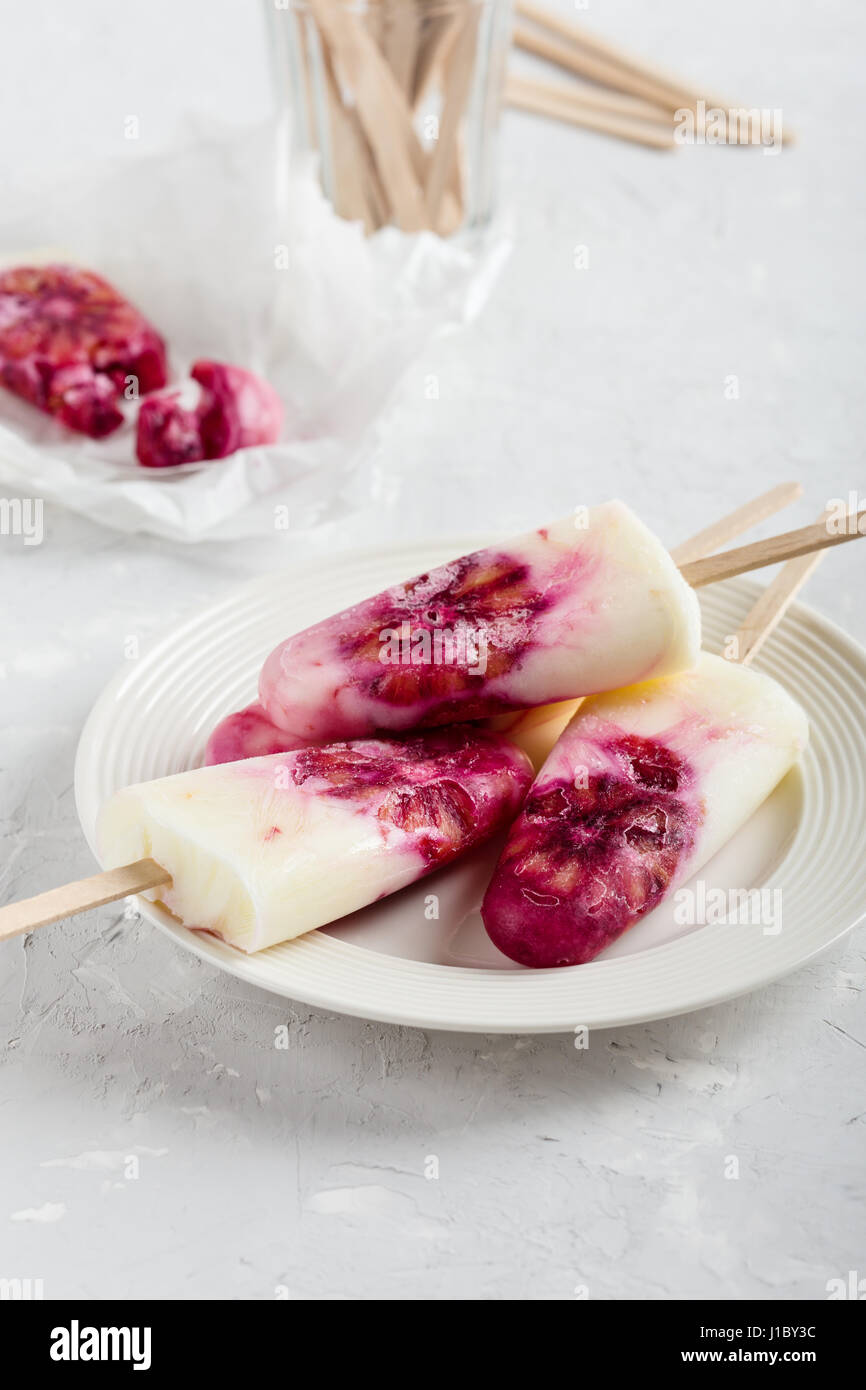 Yogurt fatto in casa ice pops decorate con sangue fettine di arancia sulla piastra bianca su di colore grigio chiaro nella tabella Foto Stock