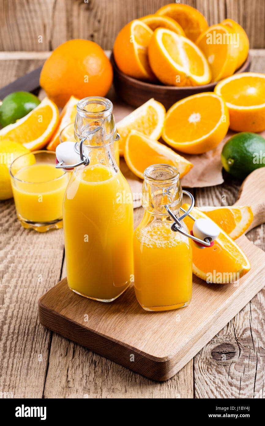 Spremuta di arancia fresca in bottiglie contro lo sfondo di agrumi freschi Foto Stock