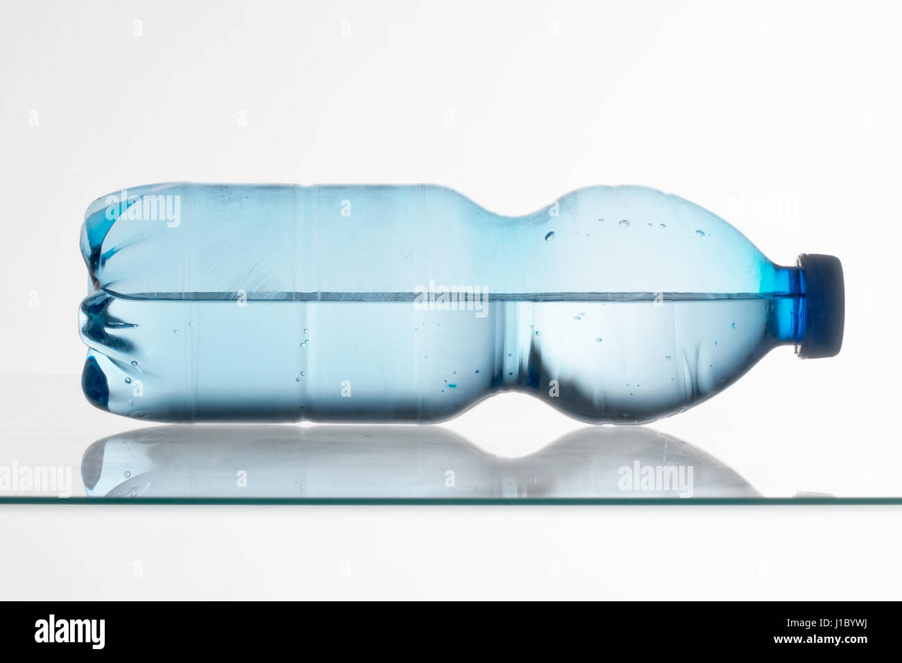 Plastica blu bottiglia d'acqua giacente sul ripiano in vetro. Mezzo pieno o mezzo vuoto. Foto Stock