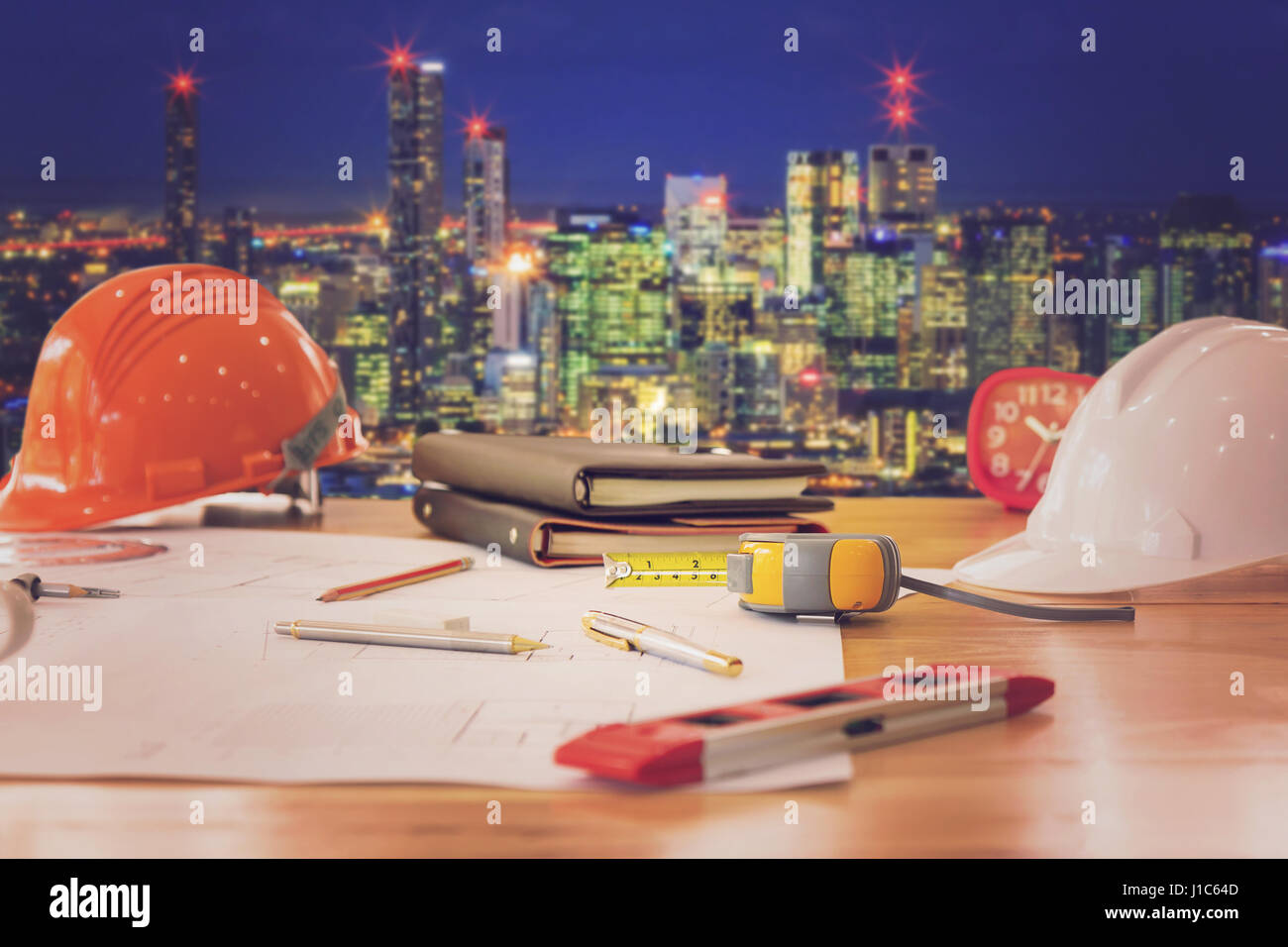 Concetto di architetto, architetti ufficio e blueprint con la città sullo sfondo di notte Foto Stock
